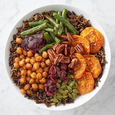 a white bowl filled with nuts, dried fruits and veggies on top of a marble table