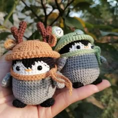 two small crocheted penguins wearing hats and scarves are held in the palm of someone's hand