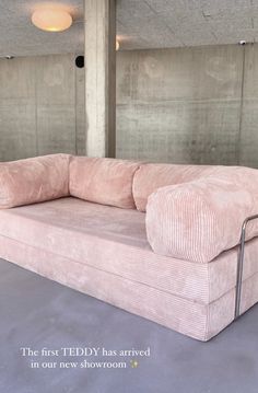 a pink couch sitting in the middle of a room with concrete walls and flooring