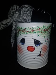 a tin can with a face painted on it and a bow hanging from the handle