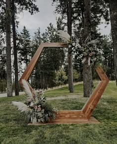 a wooden frame with flowers and feathers on it in the grass next to some trees