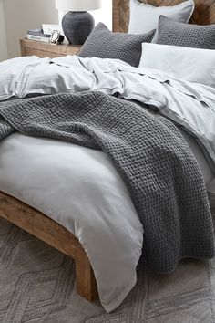 a bed with white sheets and grey blankets