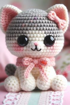 a small crocheted cat sitting on top of a pink and white bed sheet