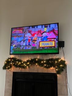 a flat screen tv mounted above a fireplace with christmas garland and lights on the mantle