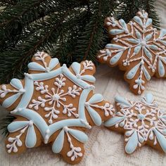 three decorated gingerbreads sitting next to a christmas tree branch with snowflakes on them