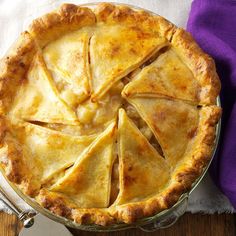 a pie sitting on top of a wooden table next to a purple napkin and fork