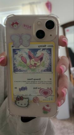 a person holding up a cell phone with hello kitty stickers on the back of it