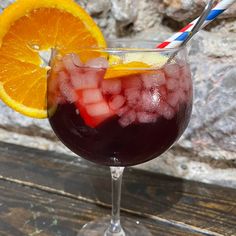 a glass filled with liquid and ice next to an orange slice on top of a wooden table