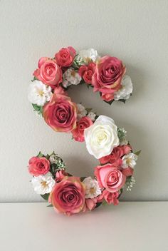 the letter s is made up of flowers and greenery on a white surface with a gray wall in the background