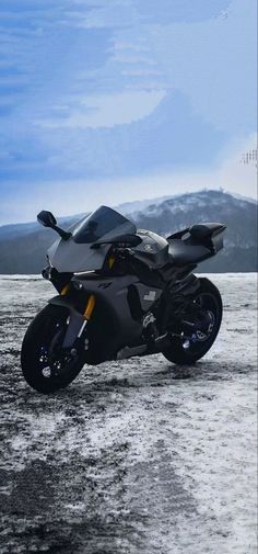 a black motorcycle parked on top of a sandy beach next to mountains in the background