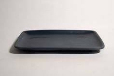 an empty black plate sitting on top of a white tableclothed surface with no one around it