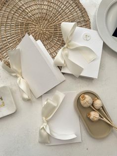 some white cards with bows on them next to plates and utensils in front of a wicker basket