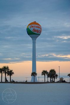 a tall water tower sitting on top of a sandy beach next to palm tree covered trees