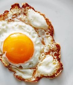 an egg is in the middle of some bread on a white plate and it appears to be fried