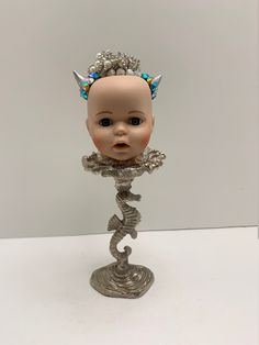 a baby doll with horns on it's head is sitting in a silver stand