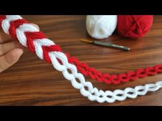 someone is crocheting a red and white ribbon on a wooden table next to yarn