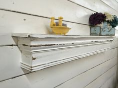 a white shelf with some vases and flowers on it's ledge next to a wall