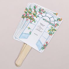 a hand fan with flowers on it sitting on top of a white table next to a pink wall