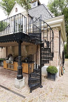 a black spiral staircase in front of a brick house with an outdoor kitchen and dining area