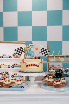 a table topped with cakes and cupcakes covered in frosting next to a checkered wall