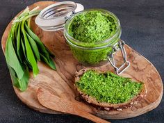 a wooden cutting board topped with bread covered in green pesto next to a jar of pesto