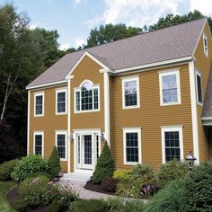 a large brown house with white trim and windows on the front, surrounded by greenery