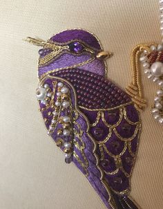 a purple and gold bird with pearls on it's head sitting next to a beaded necklace