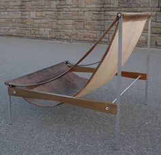 a wooden chair sitting on top of a cement floor next to a brick wall and metal frame