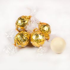 four chocolate candies wrapped in cellophane and sitting next to an egg on a white surface