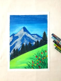 some crayons are sitting on a table next to a drawing of a mountain