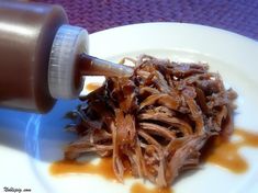 a white plate topped with meat and sauce next to a brown bottle on top of it