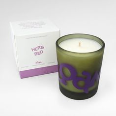 a green candle sitting next to a box on a white surface with the words herb bed printed on it