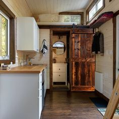 the interior of a tiny house with wood flooring and white cabinets, along with an open door