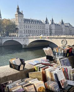 there are many books on the sidewalk by the water and buildings in the back ground