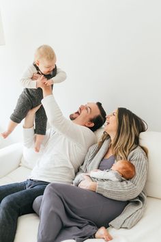 a man and woman sitting on a couch holding a baby up in the air with their hands