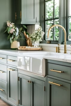 a kitchen with green cabinets and white counter tops, gold handles on the faucets