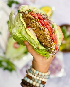 a person holding up a large sandwich with lettuce, tomatoes and other vegetables