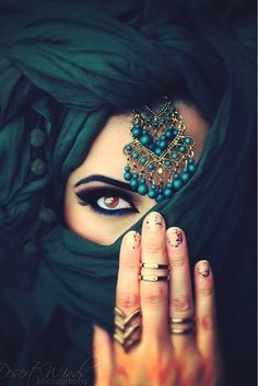 a woman with dark makeup and green eyes holding her hand to her face, wearing a black veil