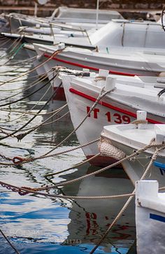 there are many small boats tied up to the dock in the water and one is white with red trim