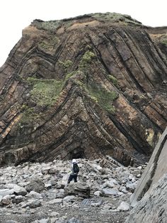 a man standing on top of a rocky hill next to a large rock formation in the distance