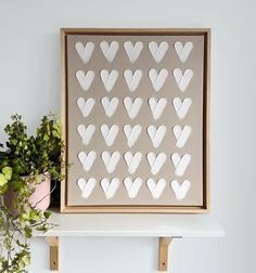 a painting with white hearts is on a shelf next to a potted plant and flowers