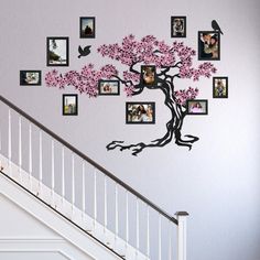 a tree with pink flowers and pictures on the wall next to a stair case in a house