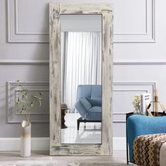 a large mirror sitting on top of a floor next to a blue chair and vase