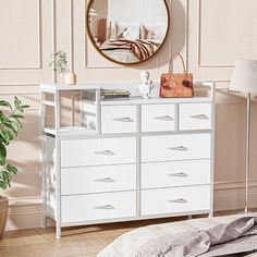 a white dresser sitting in front of a mirror on top of a wooden floor next to a lamp