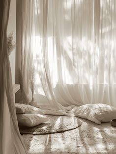 the sun shines through the sheer curtains in this bedroom with pillows and blankets on the floor