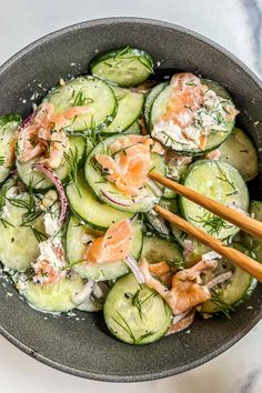 a bowl filled with cucumbers and salmon on top of a marble countertop