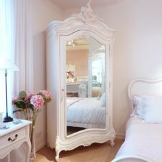 a bedroom with a white bed and a large mirror on the wall next to it