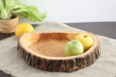 two apples in a wooden bowl on a table next to lemons and lettuce