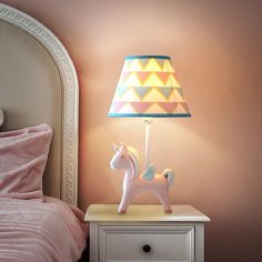 a lamp that is sitting on top of a night stand next to a bed with pink sheets