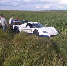 two people standing next to a white sports car in tall grass